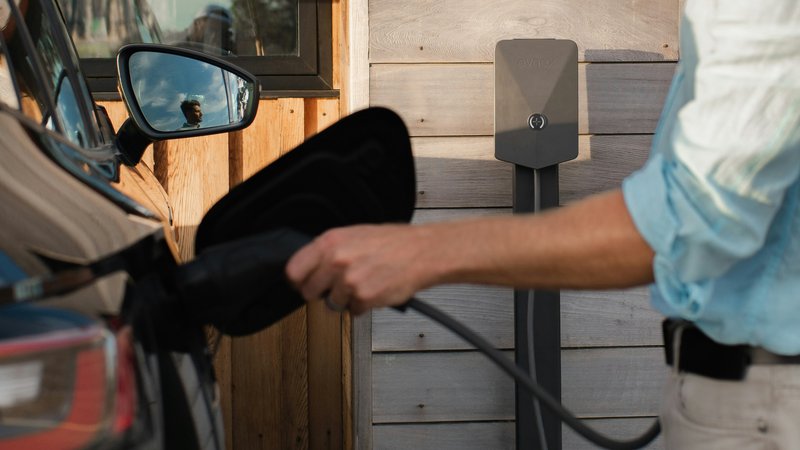Thuislaadpaal aan de muur naast een elektrische auto op een oprit