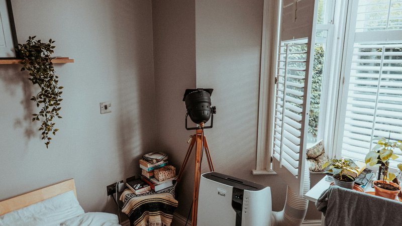 Witte mobiele airco met afvoerslang naast een raam in een woonkamer